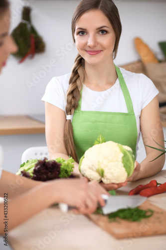 Two women are cooking fresh salad in a kitchen and having a pleasure talk. Friends and Chef Cook concept