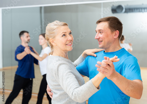 Smiling mature woman enjoying slow foxtrot in dance studio for adults..