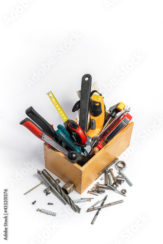 Construction tools lie in a wooden box and next to it on a white background.