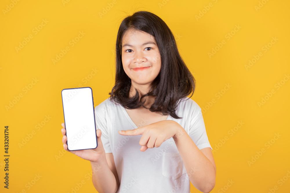 Portrait of smiling Asian teenager wears white t-shirt pointing on blank screen of smart phone isolated on yellow background, Mock up copy space Portrait of smiling Asian teenager wears white t-shirt pointing on blank screen of smart phone isolated on yellow background, Mock up copy space