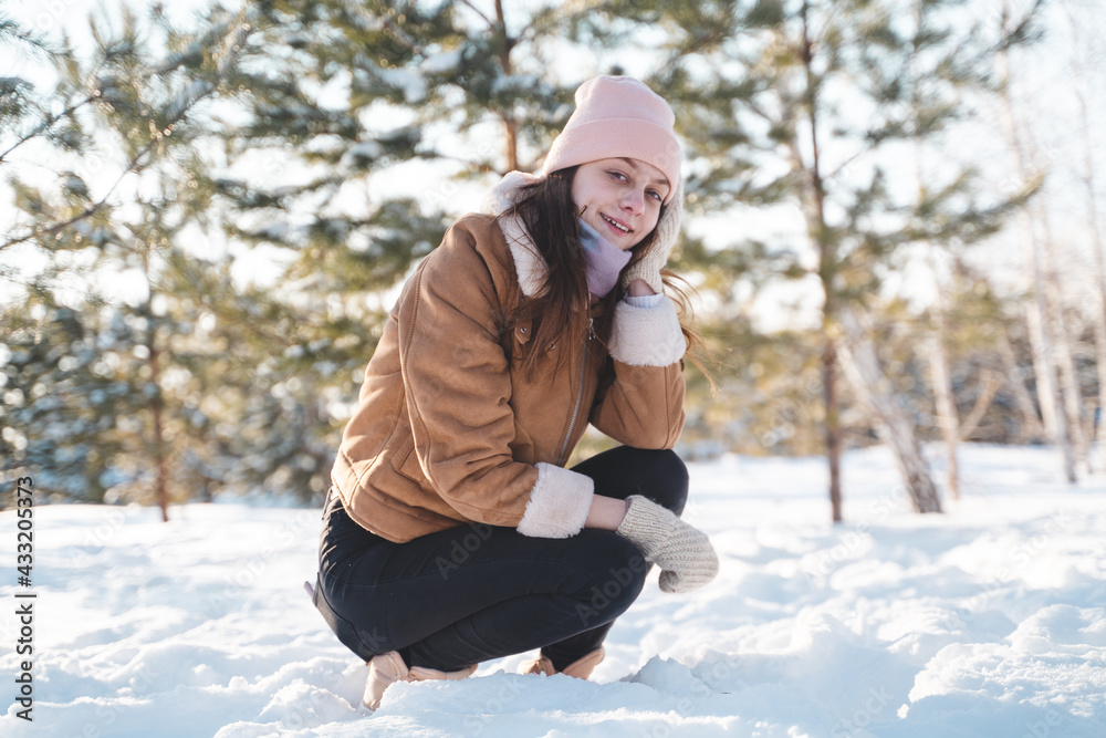 Young woman in warm clothes happy sitting in the snow and smiling