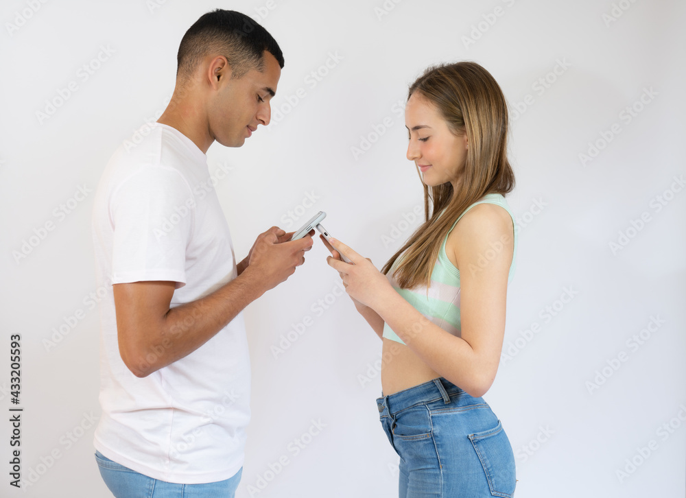 Young man and woman in casual wear standing and holding mobile phone isolated over white background Young man and woman in casual wear standing and holding mobile phone isolated over white background