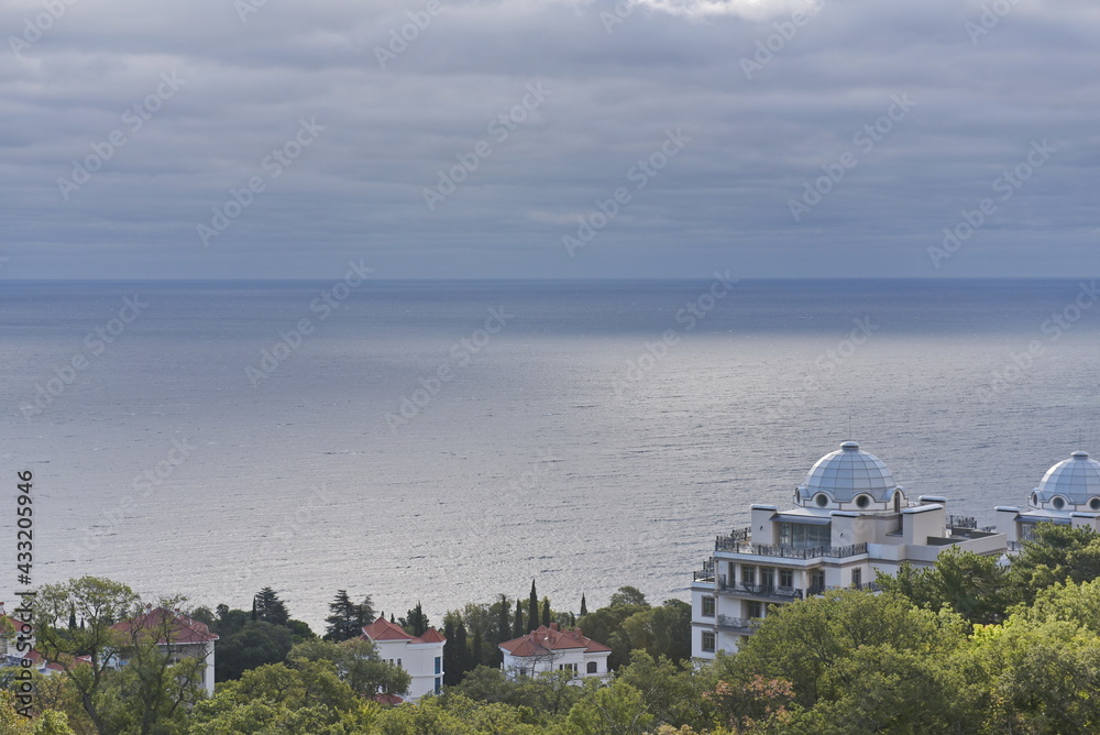Yalta, Crimea - 10.16.2015 : Different types of vegetation in a mountainous area against the background of buildings near the Black Sea coast.