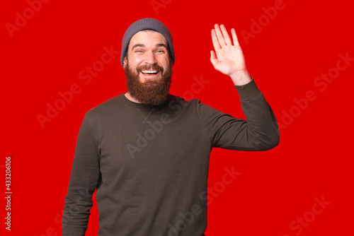 Joyful young happy man with beard making Hello gesture