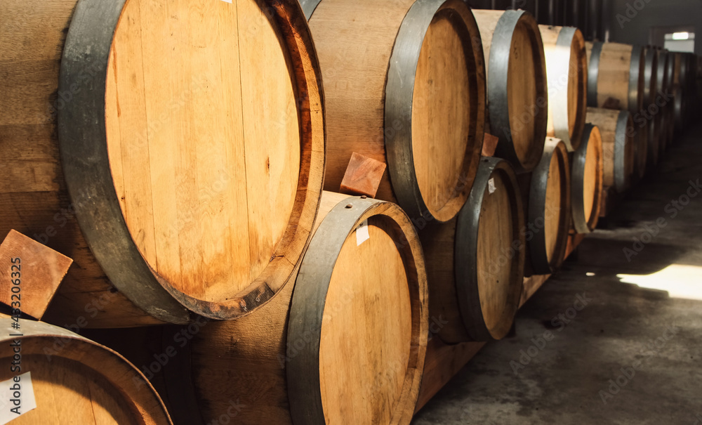 Wooden oak barrels with wine or whiskey standing inside of winery factory in the basement. Storage and fermentation cellar.