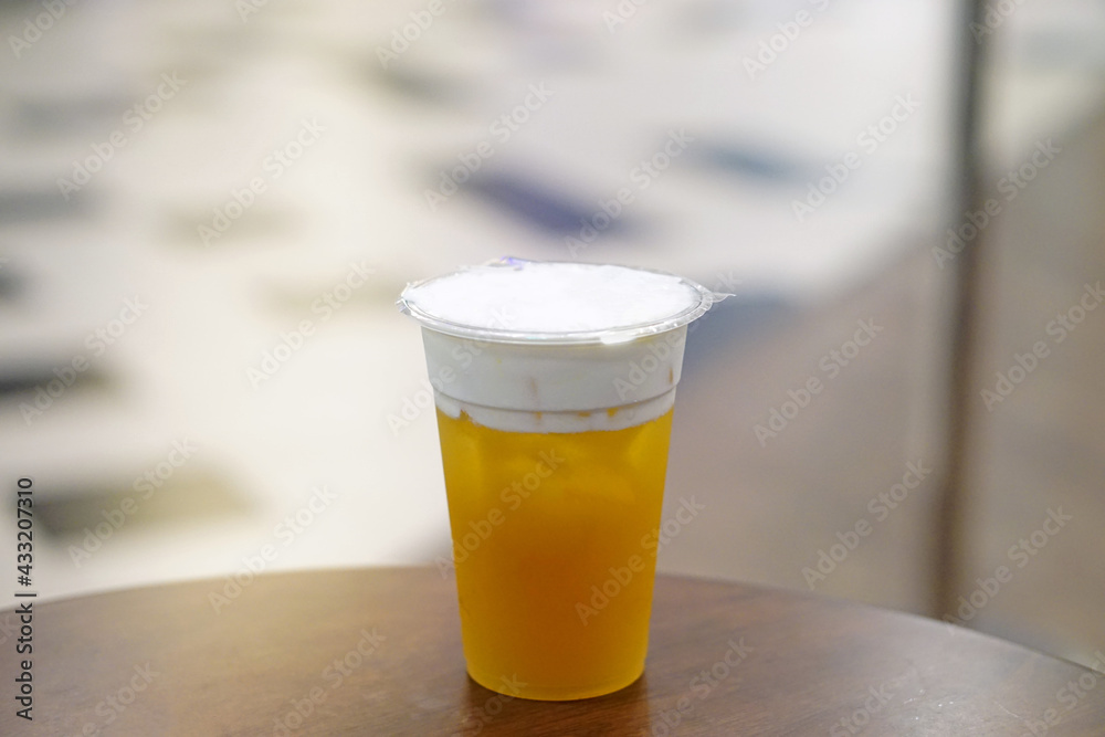 Hand holding plastic glass of iced oolong tea (also called wulong or wu long) with layer of cream cheese foam on blurred background. Hand holding plastic glass of iced oolong tea (also called wulong or wu long) with layer of cream cheese foam on blurred background.