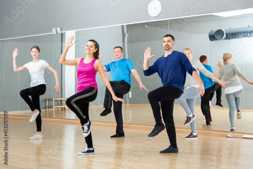 Sporty females and males doing stretching workout during group training at dance class