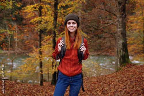 woman in autumn park with fallen leaves and backpack on her back river in the background