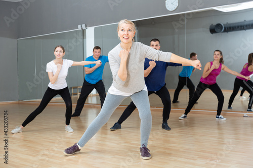 Smiling mature female doing dance workout during group classe in fitness center
