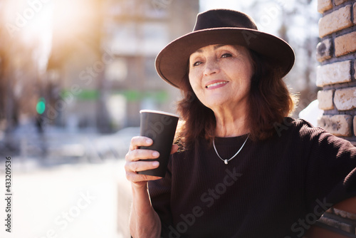 Beautiful mature elderly woman in a hat drinking takeaway coffee in a street cafe