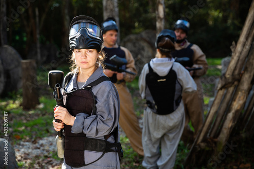 Woman and her paintball sport team in protective uniform at shooting range