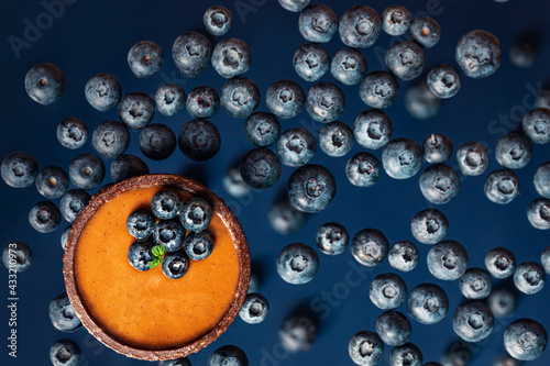 chocolate caramel tartlet with blueberries in above view on the blueberrie background, levitation