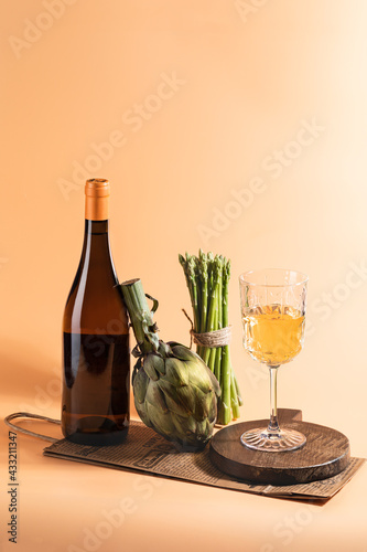 Orange wine in a glass with a bottle of dark glass on a peach background with spring vegetables in a modern still life style photo