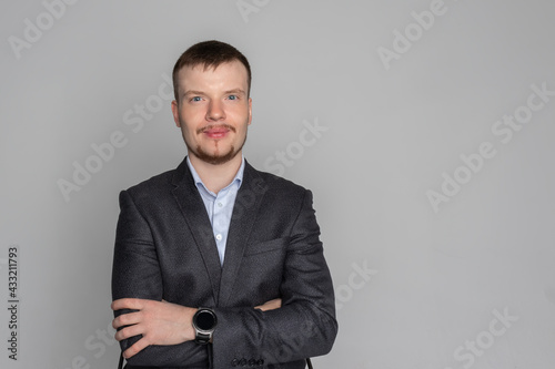 a satisfied businessman in a gray jacket crosses his arms and looks into the frame