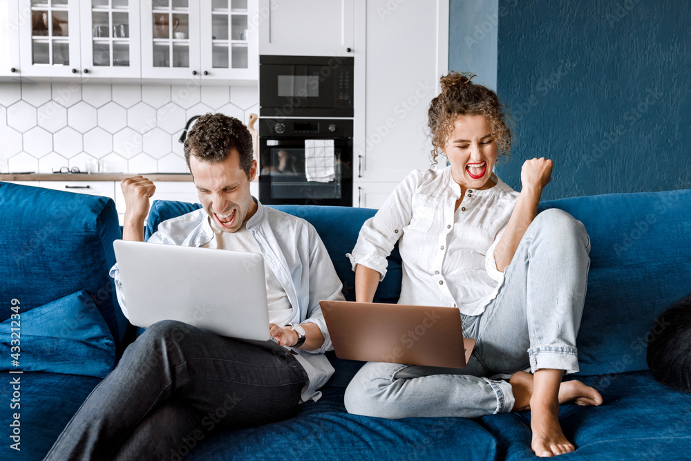 Image of successful young couple man and woman working on laptops together while sitting on coach at home. Happy spouses in love have success in new project with happiness and good emotion Image of successful young couple man and woman working on laptops together while sitting on coach at home. Happy spouses in love have success in new project with happiness and good emotion