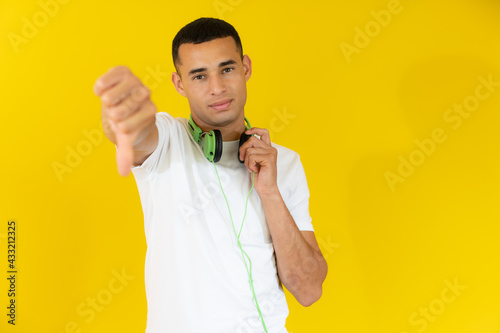 Young handsome man wearing headphones with thumb down isolated over yellow background.