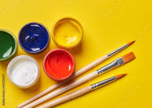 three brushes and bright cans of paint on a yellow background