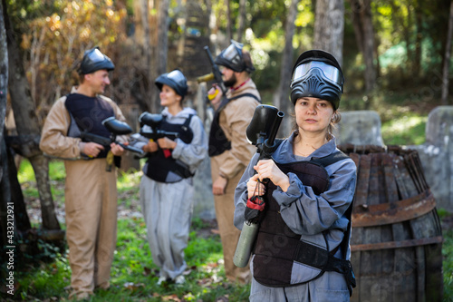 Portrait of female paintball sport player holding shooting gun and her team on background © JackF