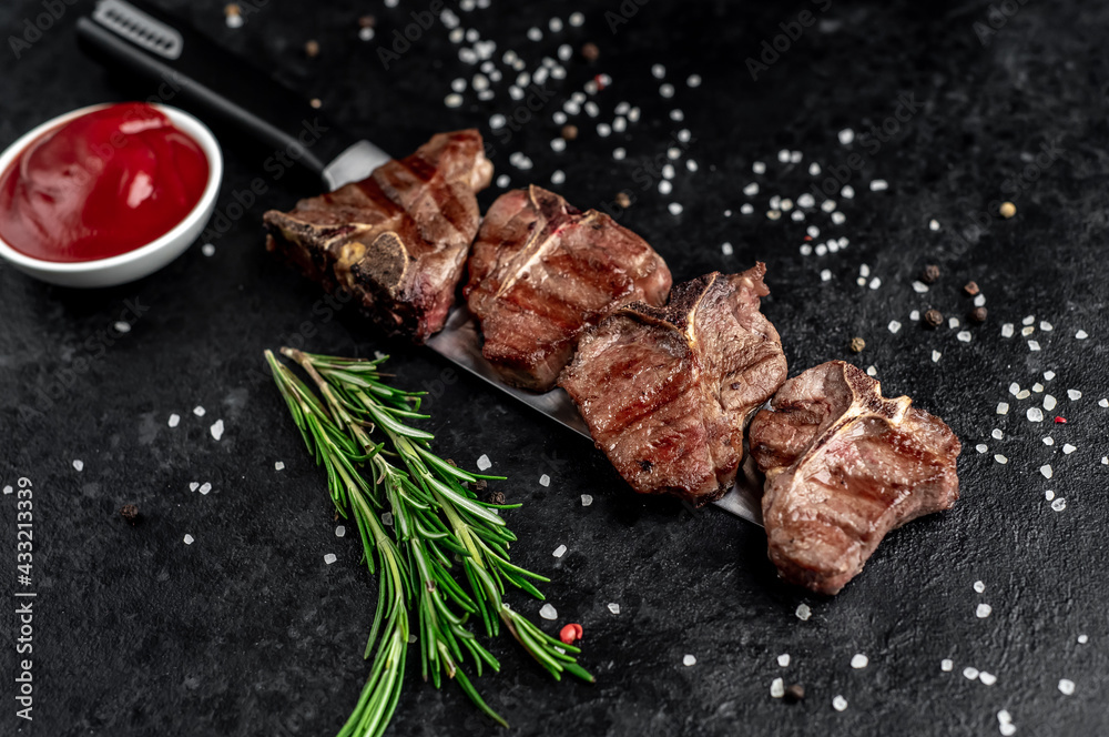 several mini Grilled beef T-bone steaks on the knife on stone background