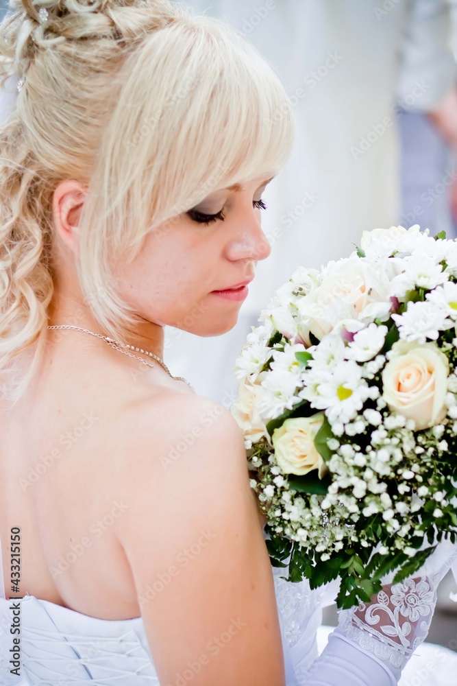 Obraz premium A blonde bride with flowers stands with her back to the viewer