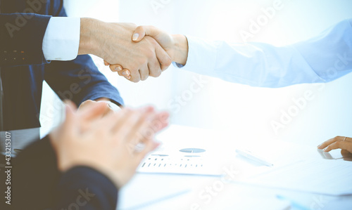 Businesspeople or lawyers shaking hands finishing up a meeting in blue toned office , close-up. Success at negotiation and handshake concepts