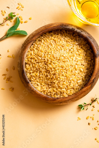 Dry uncooked bulgur in a wooden bowl on a beige background top view. Healthy food, Middle Eastern food. Free space for text