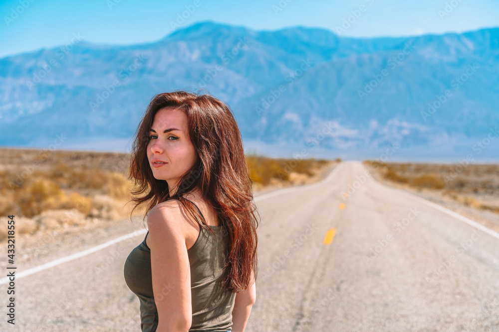 Beautiful young woman with long hair walks along a picturesque empty road in Death Valley overlooking the mountains, USA