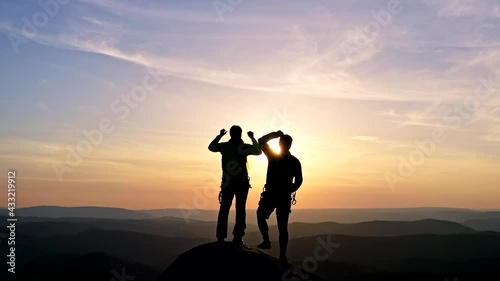 Silhouettes of a happy young couple on top of a mountain triumphantly raising their hands in the air