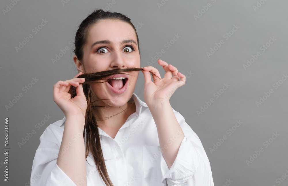  young woman in a white shirt is happy and fooling around on a gray background