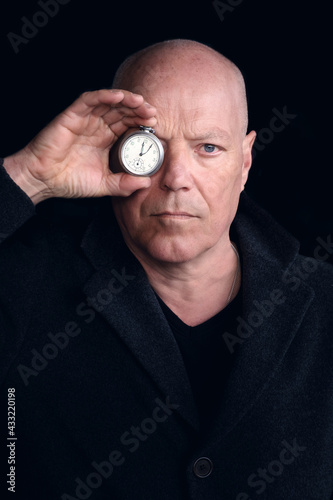 portrait of man in his 50s holding pocket watch to his eye