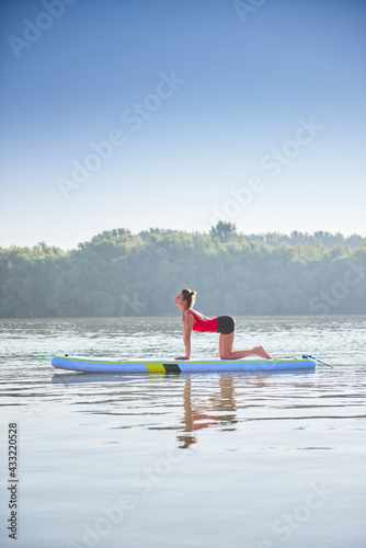 Woman meditating and practising yoga in a cow pose during sunrise on a paddleboard