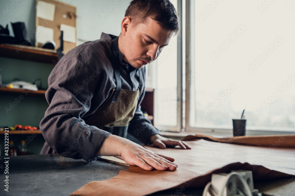 Before making shoes out of leather, a young guy lays them out on the table in the workshop Before making shoes out of leather, a young guy lays them out on the table in the workshop