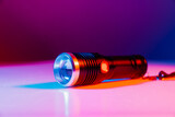 A small black flashlight in colored lighting. 
