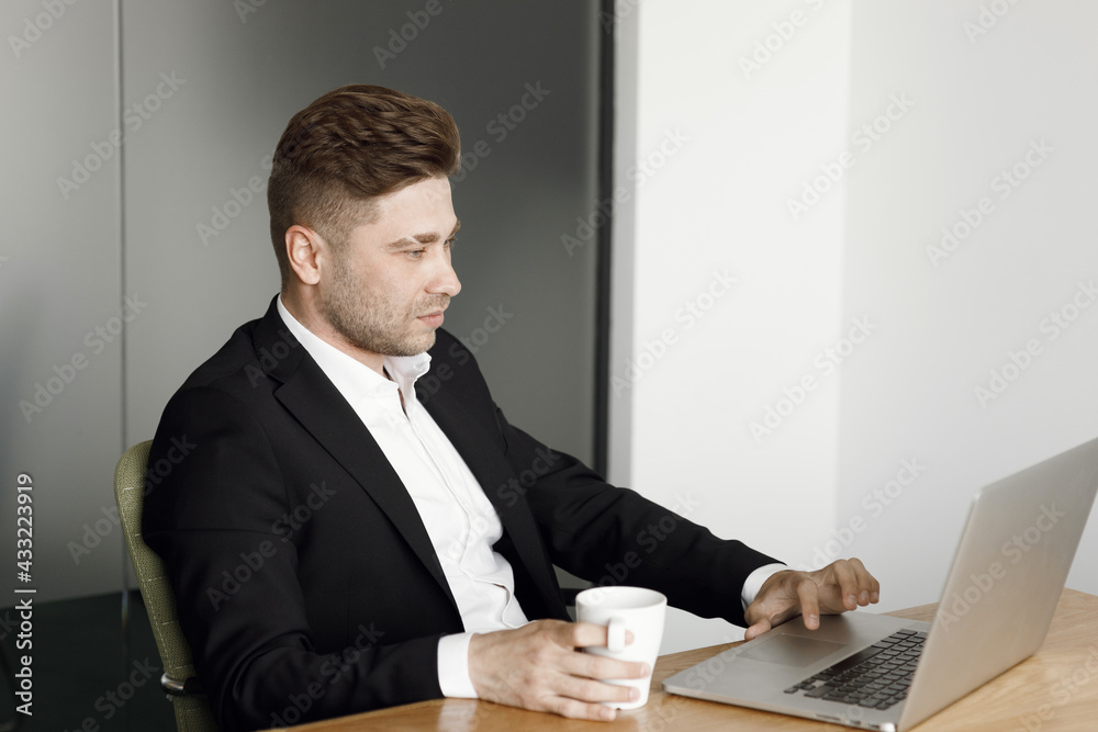A handsome businessman working with a laptop in the office. A man sits at a table and works with a cup of coffee. A handsome businessman working with a laptop in the office. A man sits at a table and works with a cup of coffee.