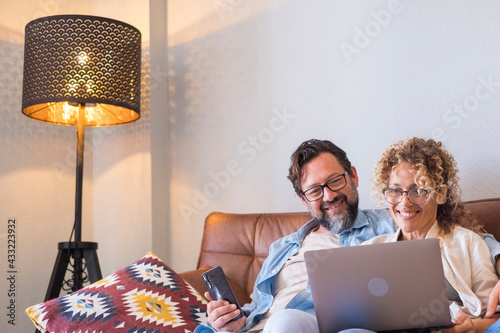 Portrait of two people man and woman enjoy technolofy connection toether with laptop and phone smiling and watching the computer - happy cheerful couple at home sitting on the sofa at work photo