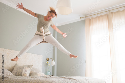 Happy young woman is smiling jumping on bed in the morning wake up - happy female people young adult have fun inthe bedroom with joy - window light and great lifestyle lady single