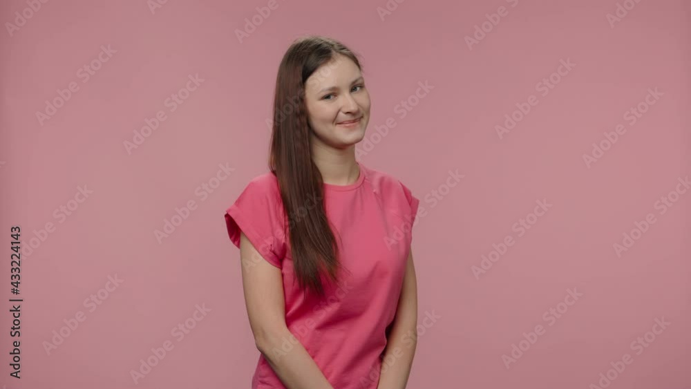 Portrait of fashion model coquettishly looking at camera and smiling. Young brown haired woman with long hair in pink t-shirt poses on pink studio background. Close up. Slow motion ready 59.94fps.