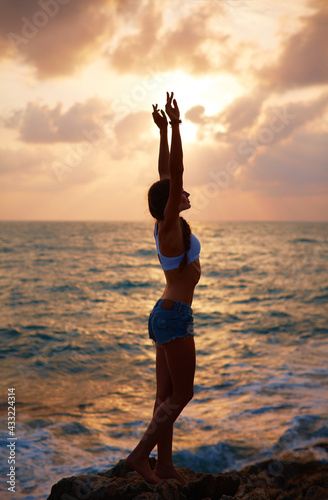Yoga at dawn. The girl meets the sunrise at sea. The beginning of the day. Happy morning. Sports, healthy lifestyle.