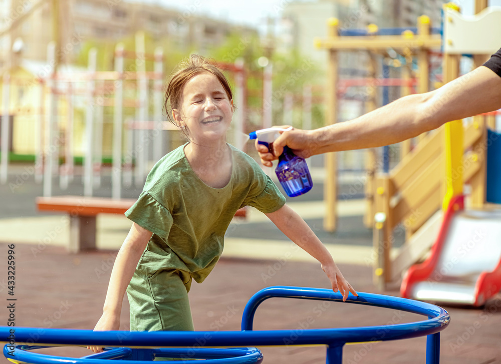 Naklejka premium Dad jumps out with water of the sprayer on his daughter on a hot weather