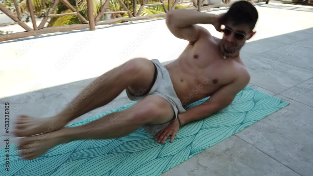Young man doing oblique leg bends on balcony overlooking ocean and palm trees.
