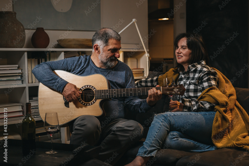 middle age couple relaxing together at home. drinking wine and playing guitar and singing
