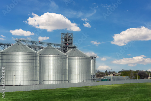 Scenic view of big modern steel agricultural grain granary silos cereal bin storage warehouse against blue sky. Agribusiness farmland rural industry silo landscape scene. Mill store farm facility