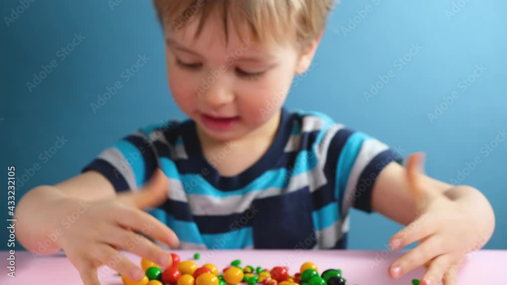 Cute little child boy playing with colorful chocolate candies on blue background. Sweets and unhealthy food. Happy childhood concept. Cute little child boy playing with colorful chocolate candies on blue background. Sweets and unhealthy food. Happy childhood concept.