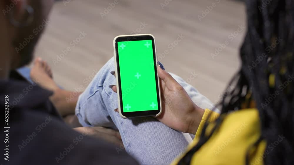 Green screen on smartphone. Man and woman having fun on sofa with cell phone for internet and film or movie. Happy people and technology at home