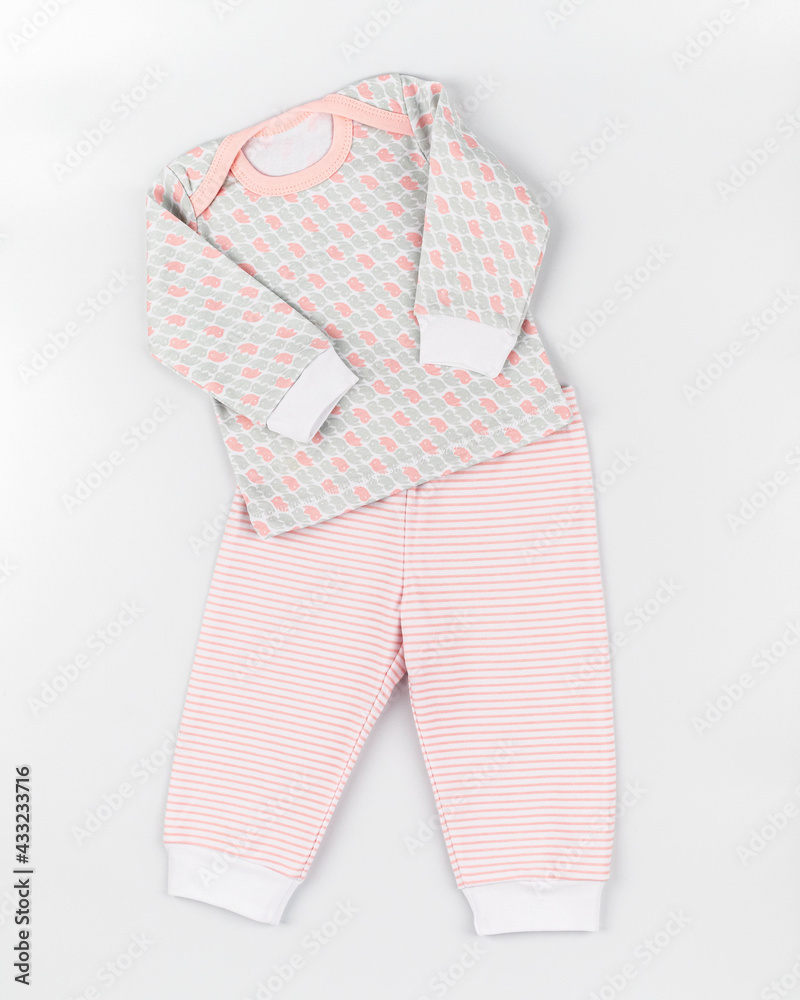 Pajamas for the baby. Laid out clothes on a white background, top photo, top view, dynamic photo. Home suit of blouse and trousers for girls in pink color made of natural knitted cotton.