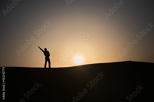 A man stands on a desert dune and makes a movement like Michael Jackson. Do you know the feeling when everything is possible? It's a great feeling. Off to the desert ;-) Sunset. Normal perspective. 