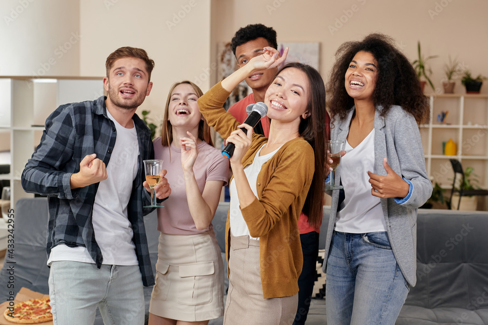 Party fun. Young asian girl holding microphone and singing while playing karaoke with best friends at home. Group of people drinking, having fun together Party fun. Young asian girl holding microphone and singing while playing karaoke with best friends at home. Group of people drinking, having fun together