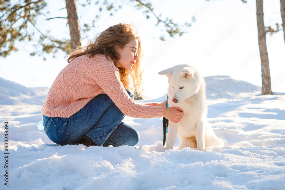 A curly-haired girl walks with a white akita in a snowy forest.