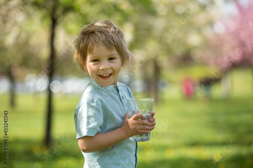 Beautiful blond child  boy  drinking water in the park on a hot day