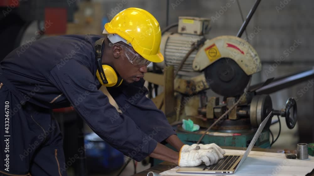african american Industrial Engineer in Hard Hat Wearing safety goggles using laptop computer in Industry Manufacturing Factory. black Factory worker using a notebook with an engineering software african american Industrial Engineer in Hard Hat Wearing safety goggles using laptop computer in Industry Manufacturing Factory. black Factory worker using a notebook with an engineering software